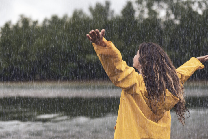 Rear view of carefree woman standing in nature with her arms outstretched during rainy day.