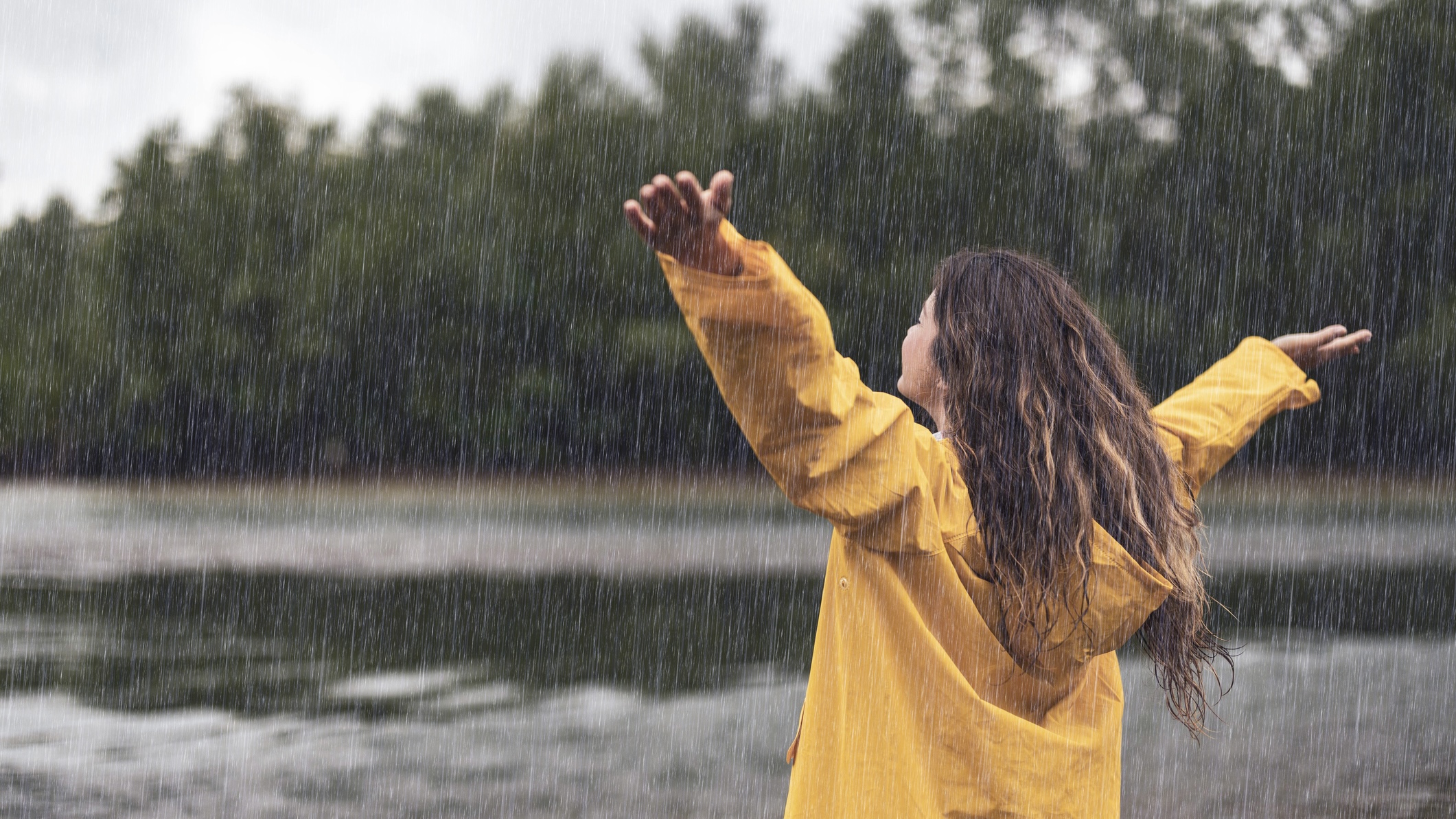 Rear view of carefree woman standing in nature with her arms outstretched during rainy day.